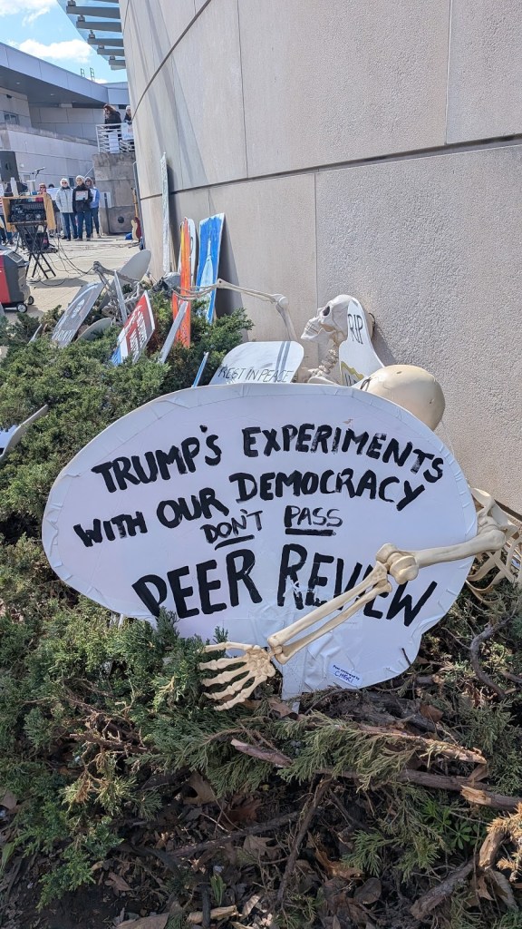 A sign in the "graveyard" reads "Trump's experiments with our democracy don't pass peer review," with a fake skeleton's arm around it